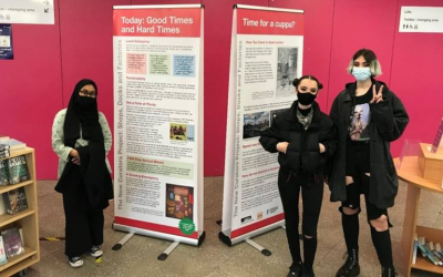 Three people stand in front of a display from Newham News Curators. 