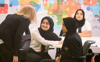 UCL staff member speaking with school pupils at a desk. 