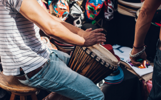 Musician sits playing a Djembe drum in a crowd of people.