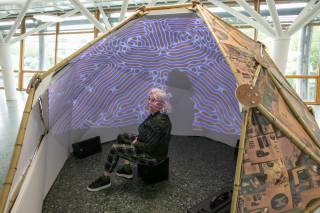 Person sits inside a cocoon like structure, inside which are projected abstract patterns