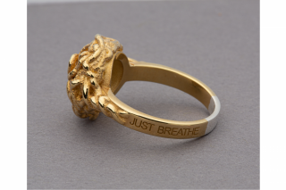 Gold ring with knotted detail. The words JUST BREATH are on the band