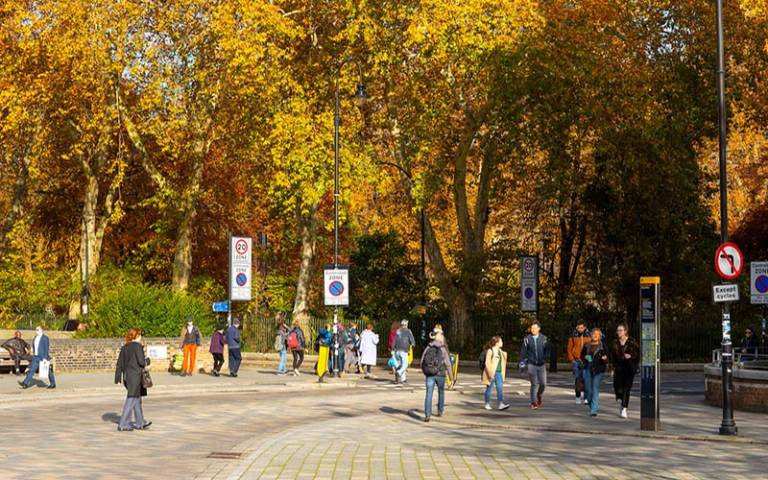 People walking on Byng Place. An Autumnal Gordon Square gardens is in the Background. © UCL Digital Media