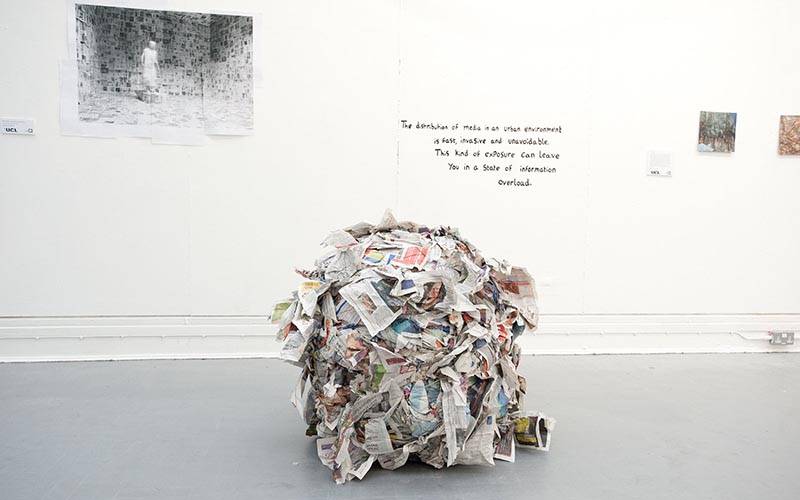 An oversized crumpled up ball of newspapers sits on a gallery floor